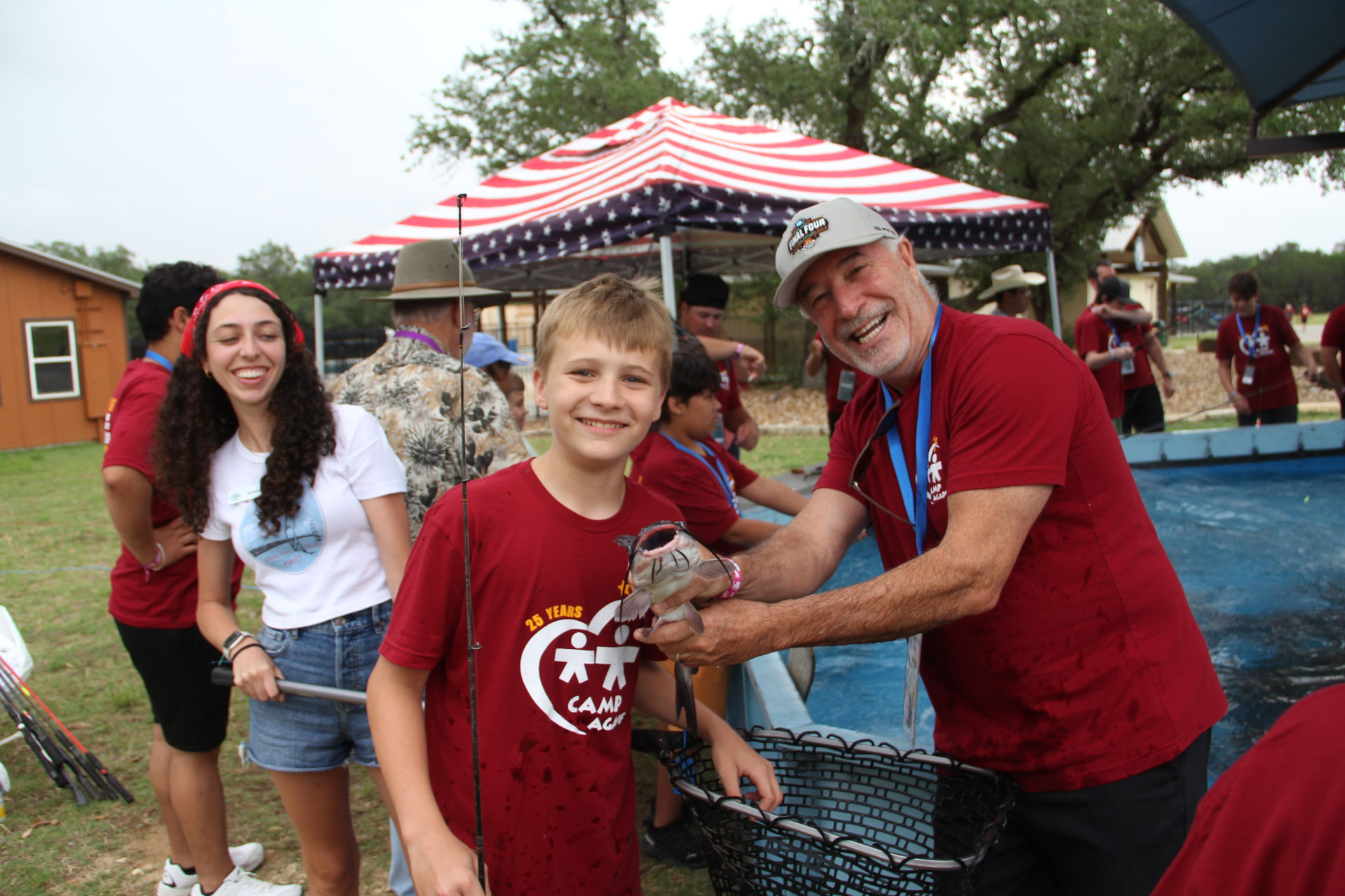 A camper proudly holds a catfish with a smiling volunteer at the fishing tank.