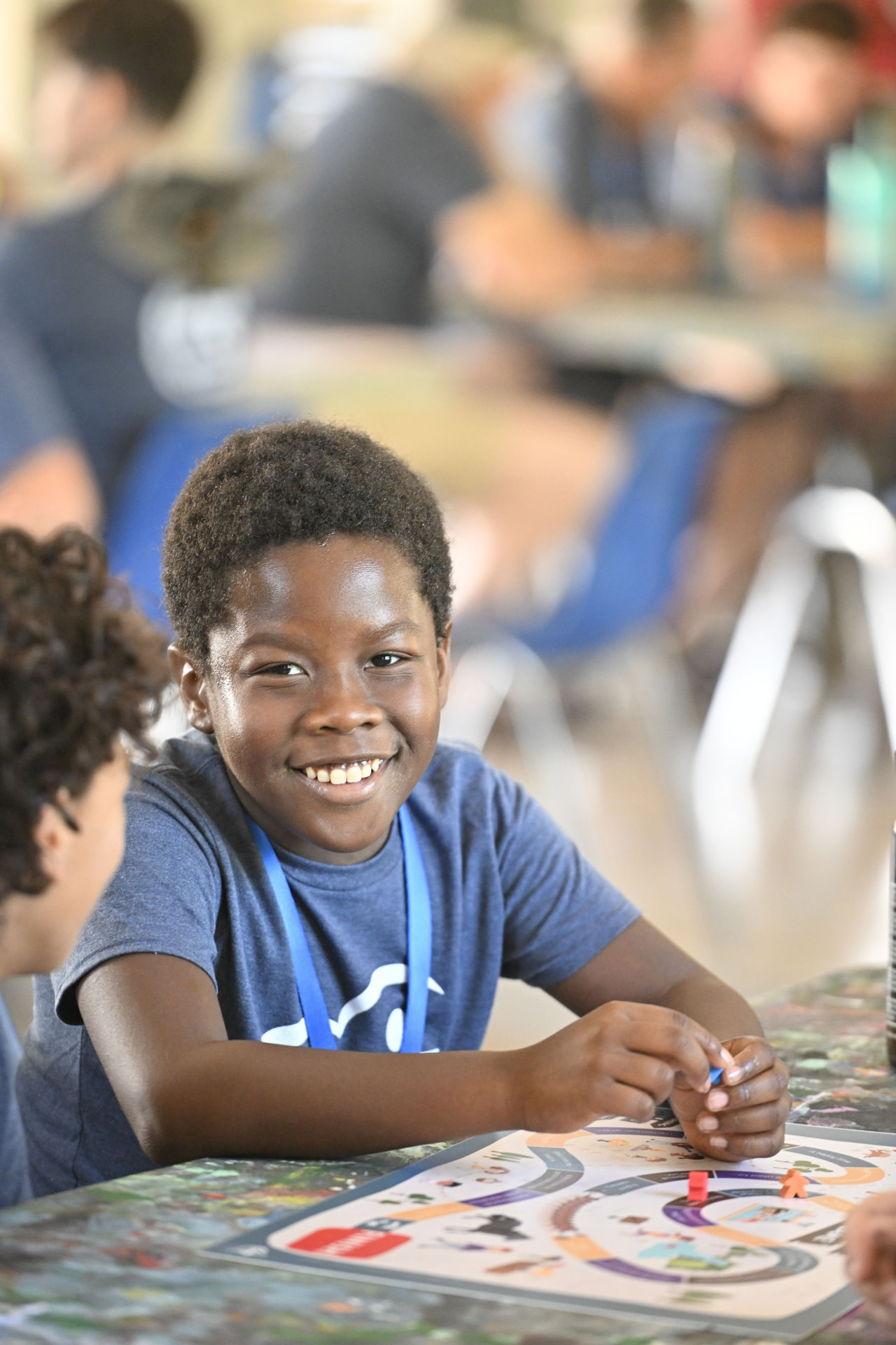 A smiling boy moves a game piece across the Memory Lane Game board at camp.