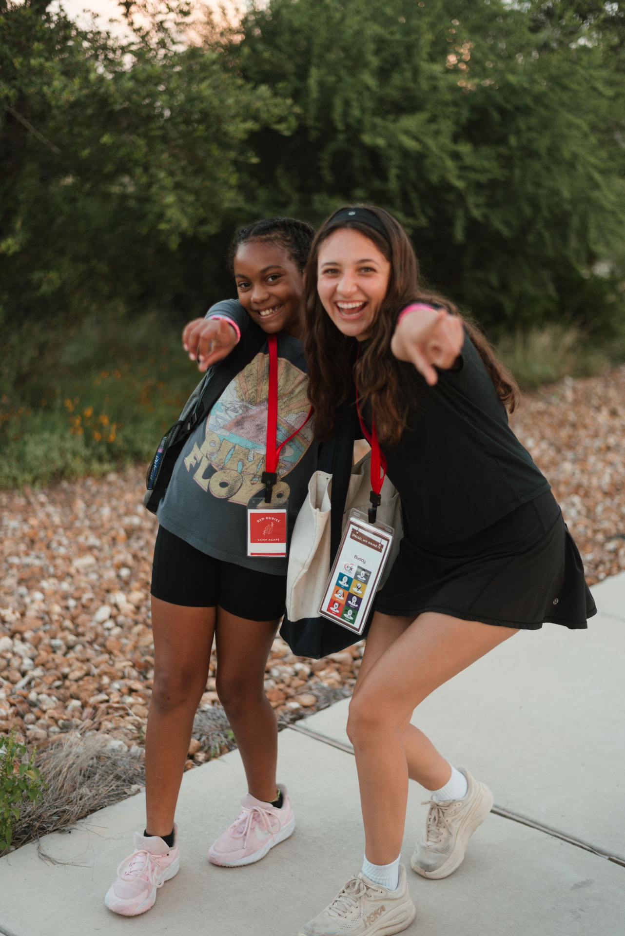 A camper and her Camp Agape buddy laugh and point at the camera on a walkway at camp.