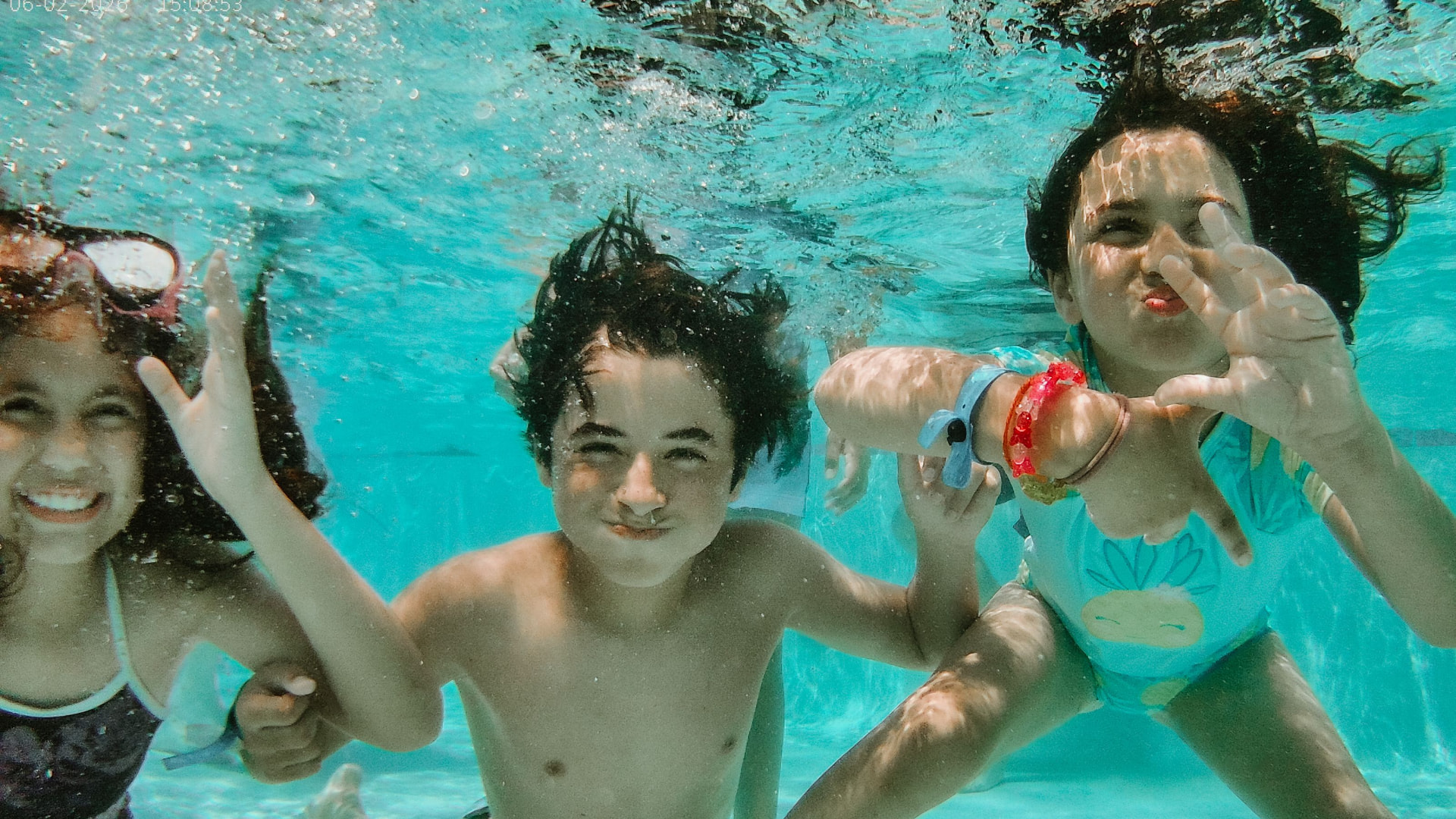 Three campers smiling and waving underwater in the camp pool.